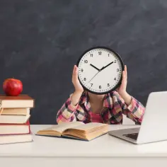 Dziecko z zegarem zamiast twarzy, stos książek, jabłko i laptop. Czas nauki, godziny pracy maj.