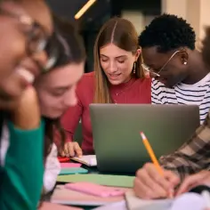 Studenci dyskutują przy laptopie, notując. Zastanawiają się, czy studia liczą się do stażu pracy, planując przyszłość.