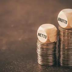 Drewniane kostki z napisami "BRUTTO" i "NETTO" na stosach monet. Zastanawiasz się, ile to netto z 31,40 brutto na umowie zlecenie?