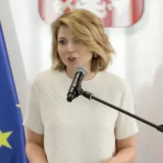 Kobieta przemawia przy mikrofonie, obok flagi UE i Polski. Jej słowa mogą dotyczyć interwencji poselskiej.