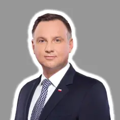 Prezydent Andrzej Duda w garniturze, z biało-czerwoną flagą na klapie. Jego uśmiech może sugerować ułaskawienie prezydenta.
