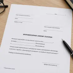 Dokument "Wypowiedzenie umowy zlecenia" leży na drewnianym biurku obok okularów i długopisu.