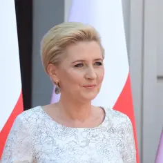 Pierwsza dama w białej sukni z kwiatowym wzorem, obok flagi Polski.