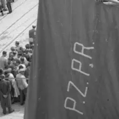 Ludzie zgromadzeni na ulicy, na pierwszym planie duża, ciemna tkanina z napisem "P.Z.P.R.".