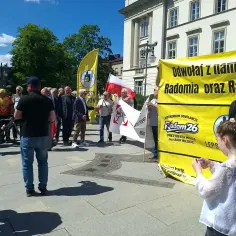 Grupa osób demonstruje pod hasłem "Odwołaj z nami Radomia oraz Radę Miejską". W tle żółty baner z napisem "Referendum odwoławcze Radom26".