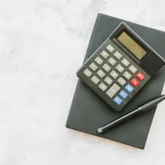 Kalkulator i długopis na czarnym notesie. Obliczanie, ile urlopu na pół etatu, to proste zadanie.