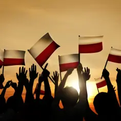 Tłum z polskimi flagami wzniesionymi ku niebu, symbol wolności i upadku komunizmu w Polsce.
