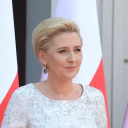Pierwsza dama w białej sukni z kwiatowym wzorem, obok flagi Polski.