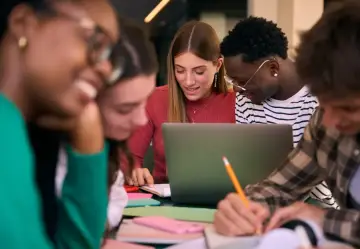 Studenci dyskutują przy laptopie, notując. Zastanawiają się, czy studia liczą się do stażu pracy, planując przyszłość.