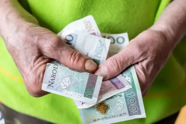Dłonie trzymają polskie banknoty: 10, 20 i 100 zł. Zastanawiasz się, ile wynosi renta?