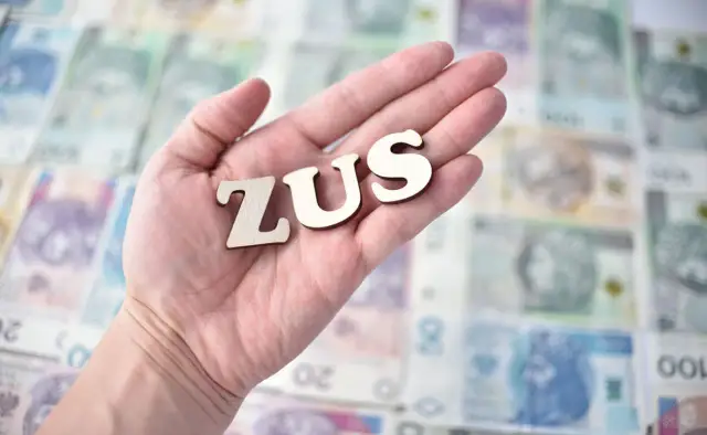 Litery "ZUS" na dłoni na tle polskich banknotów. Symbolizuje to potencjalne odszkodowanie z ZUS.